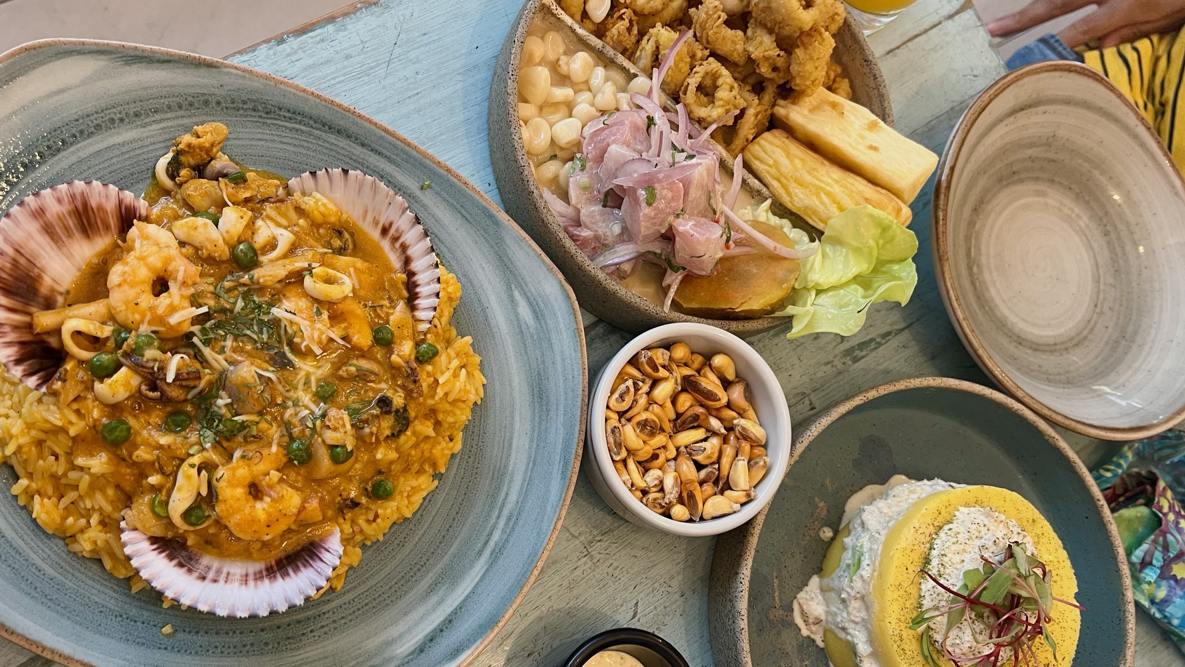 Ein Teller mit verschiedenen peruanischen Gerichten, darunter Ceviche, Reis mit Meeresfrüchten, frittierte Garnelen, und ein Kartoffeltörtchen, serviert auf stilvollen Tellern.