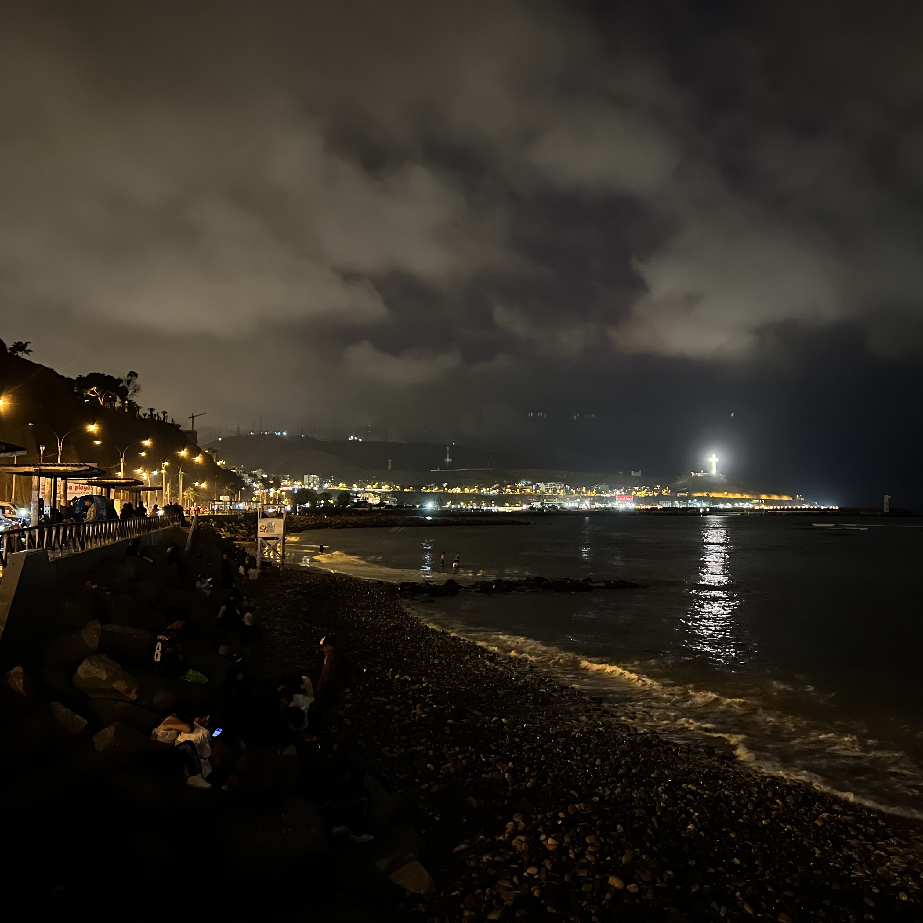 Nachtaufnahme des Küstenbereichs von Lima, Peru, mit beleuchteten Stadtlichtern und dem Meer im Vordergrund.