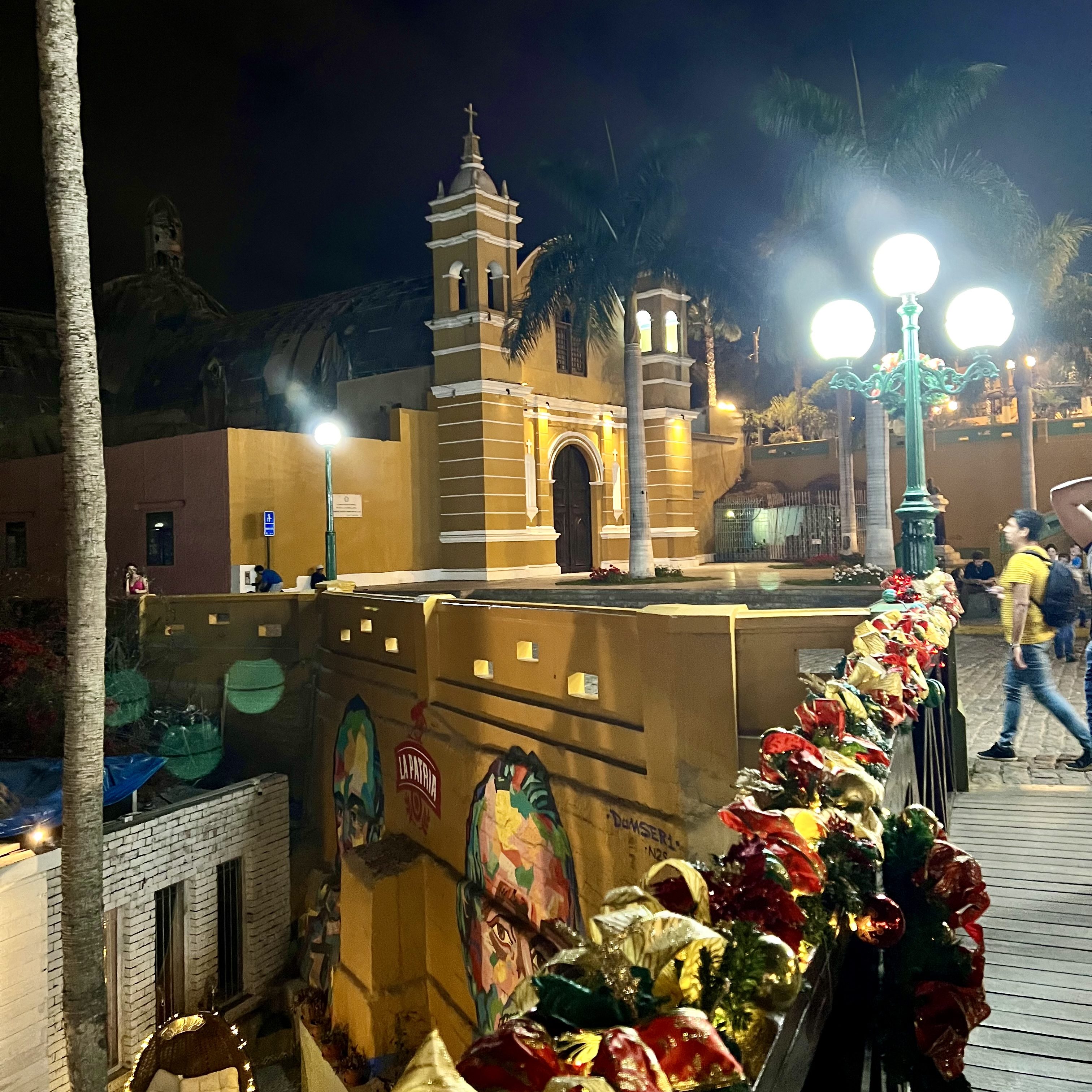 Nachtaufnahme der Puente de los Suspiros in Barranco, Lima, mit dekorativem weihnachtlichem Lichterkranz und Passanten auf der Brücke.